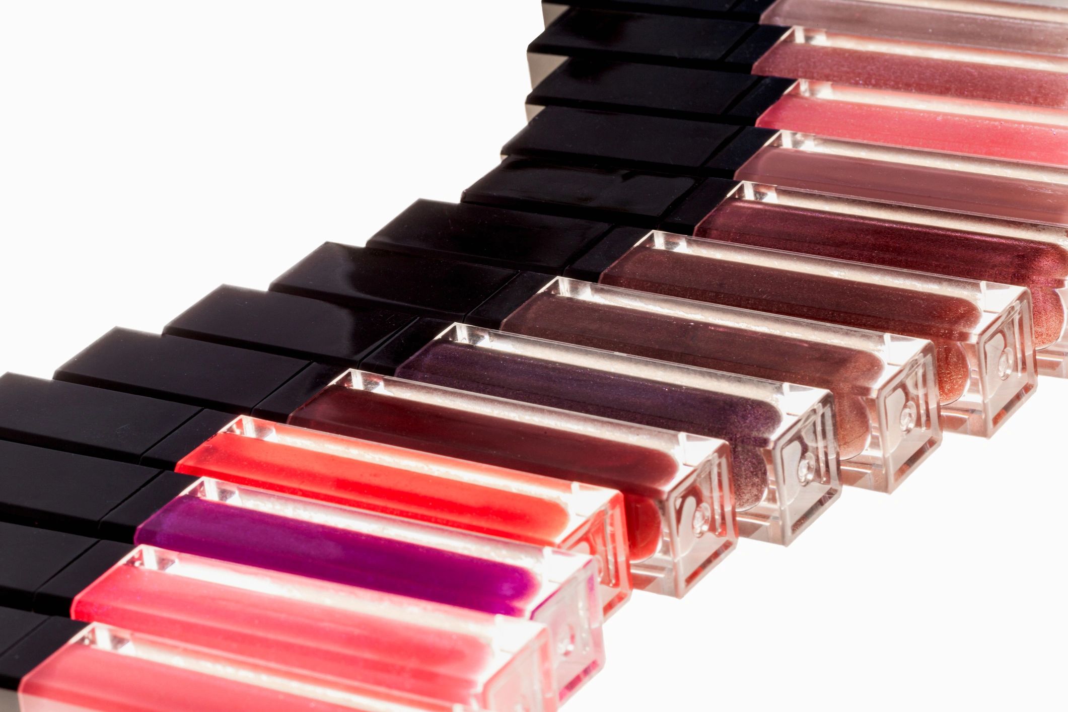 Assorted lip glosses arranged in a clean wave pattern on a white background
