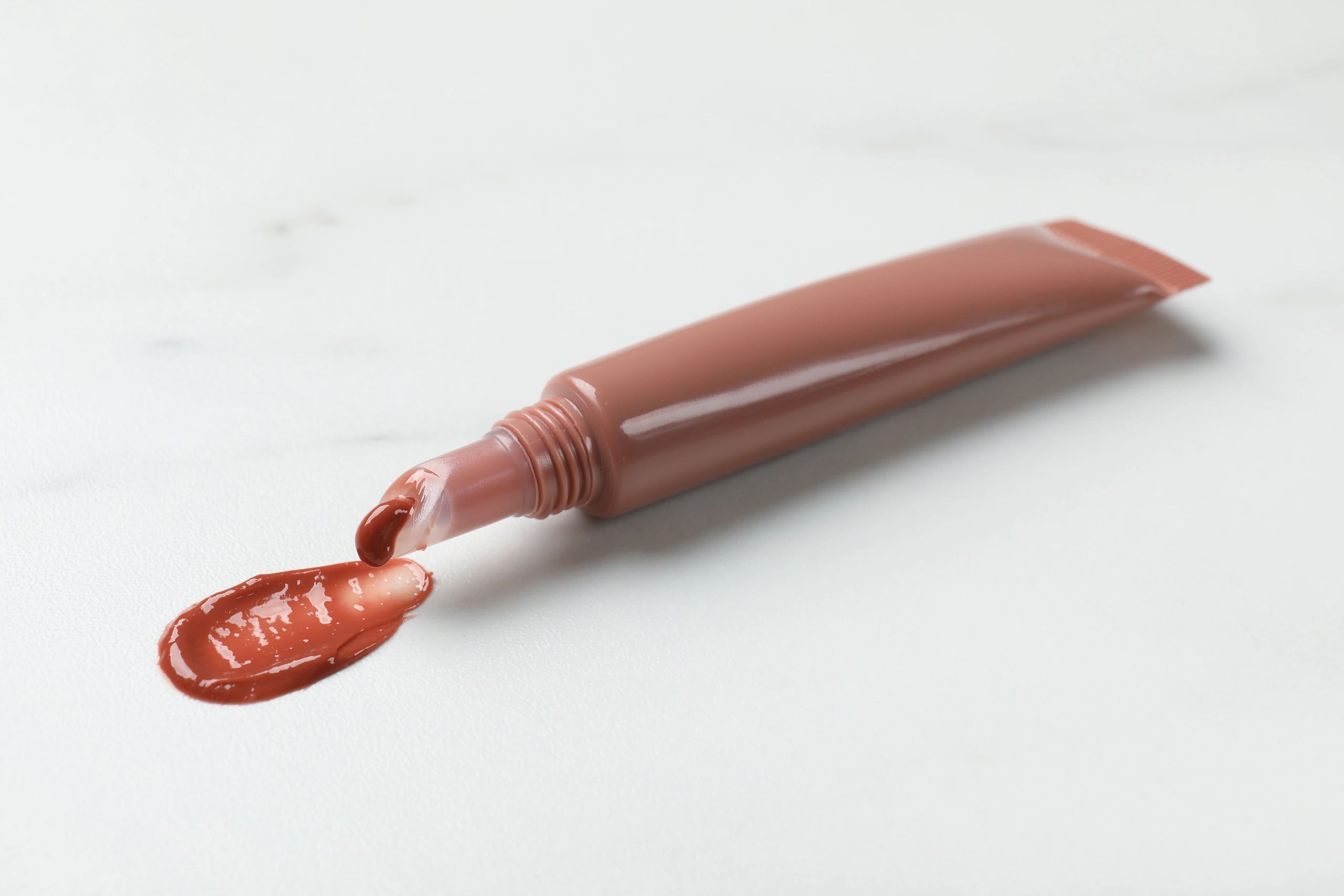 Nude vegan lip gloss and swatch on a light marble background